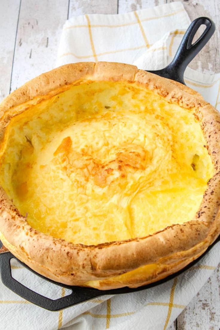 a baked dish sitting on top of a white and yellow towel next to a black frying pan