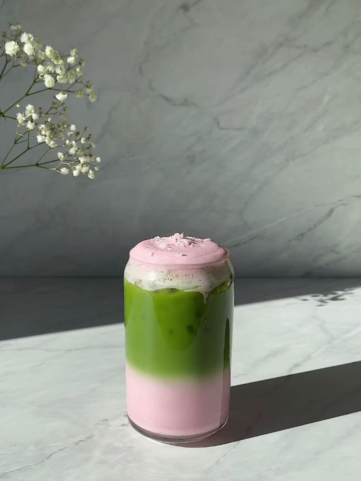 a pink and green drink sitting on top of a table next to a vase with flowers