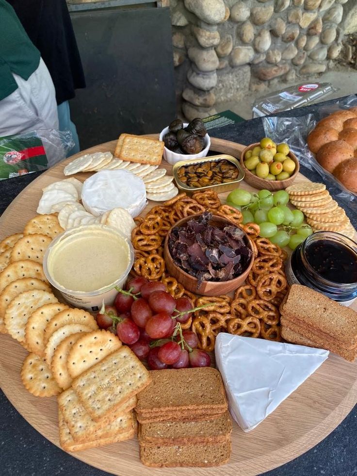 a wooden platter filled with cheese, crackers and grapes next to other snacks