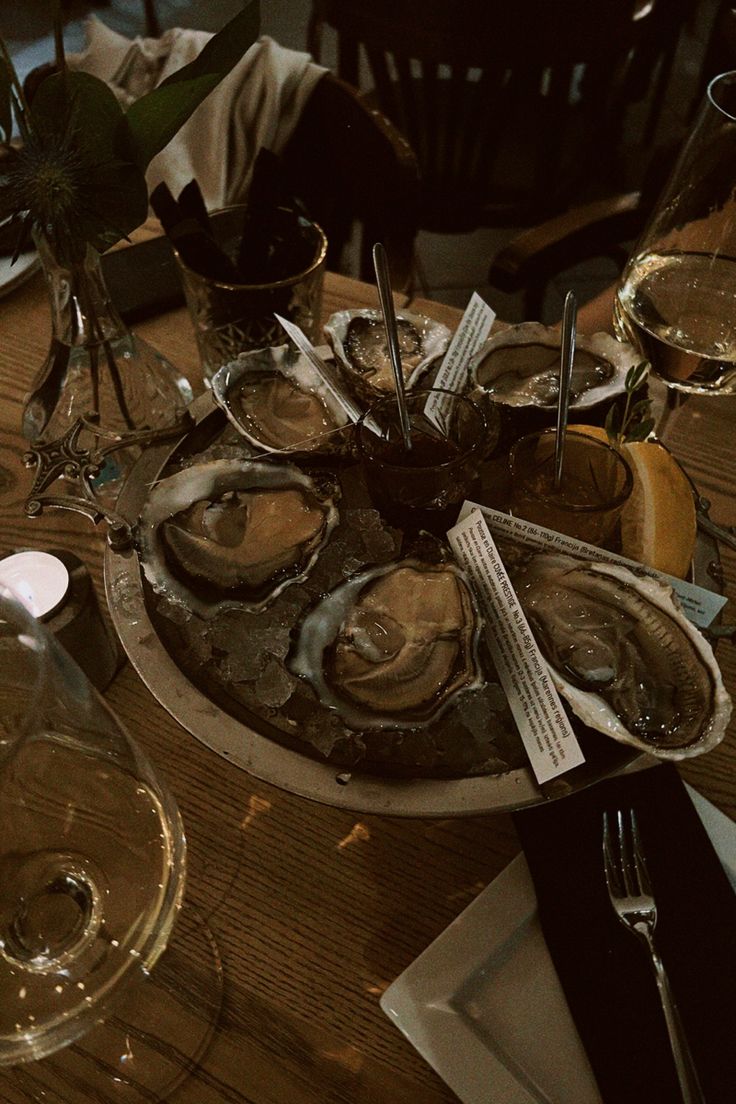 oysters on the half shell with wine glasses and utensils sitting on a wooden table