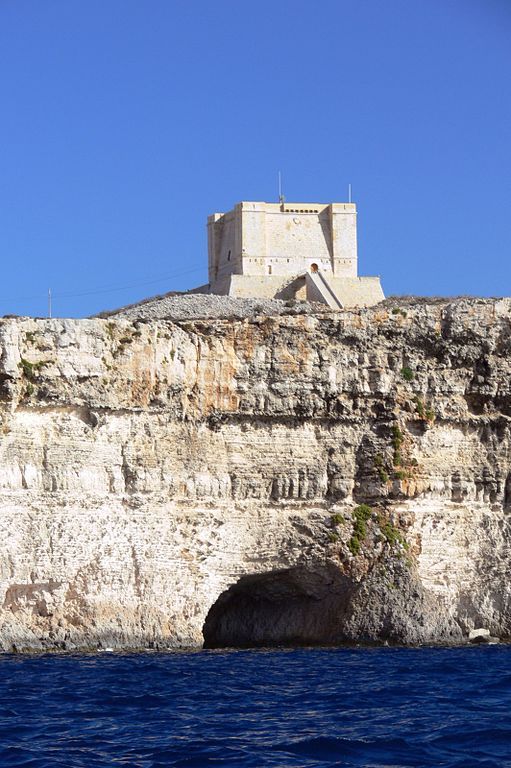 an old castle perched on top of a cliff above the blue water in front of it