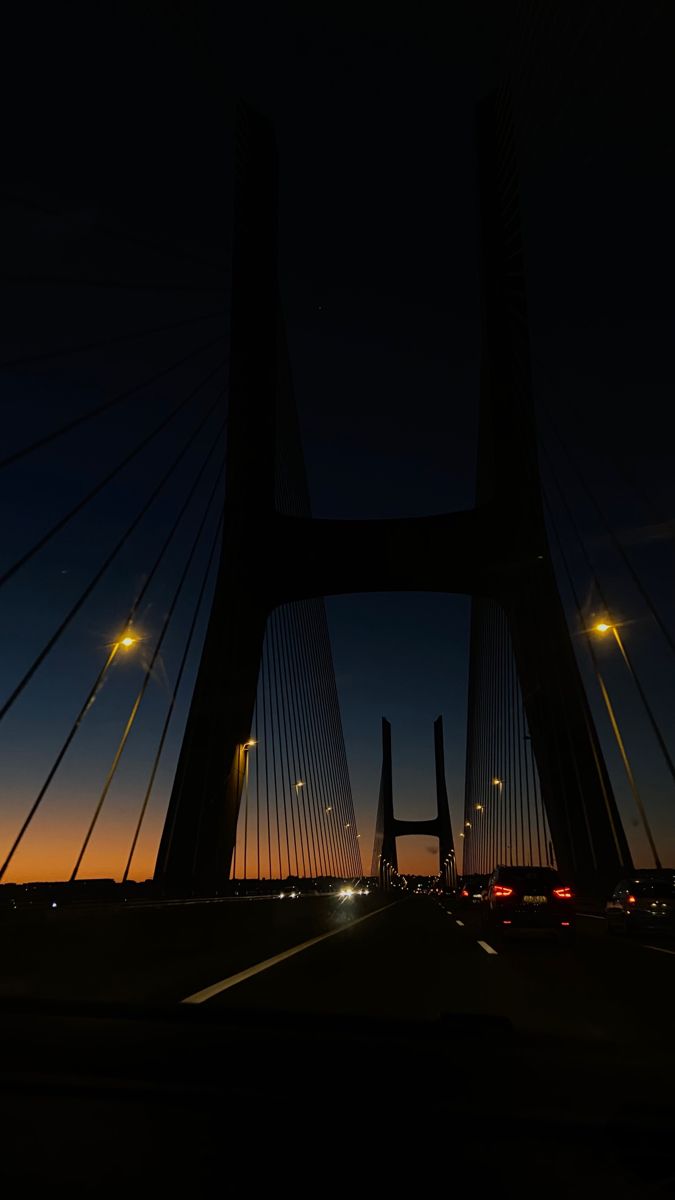 the sun is setting behind a bridge with cars driving on it and lights in the distance