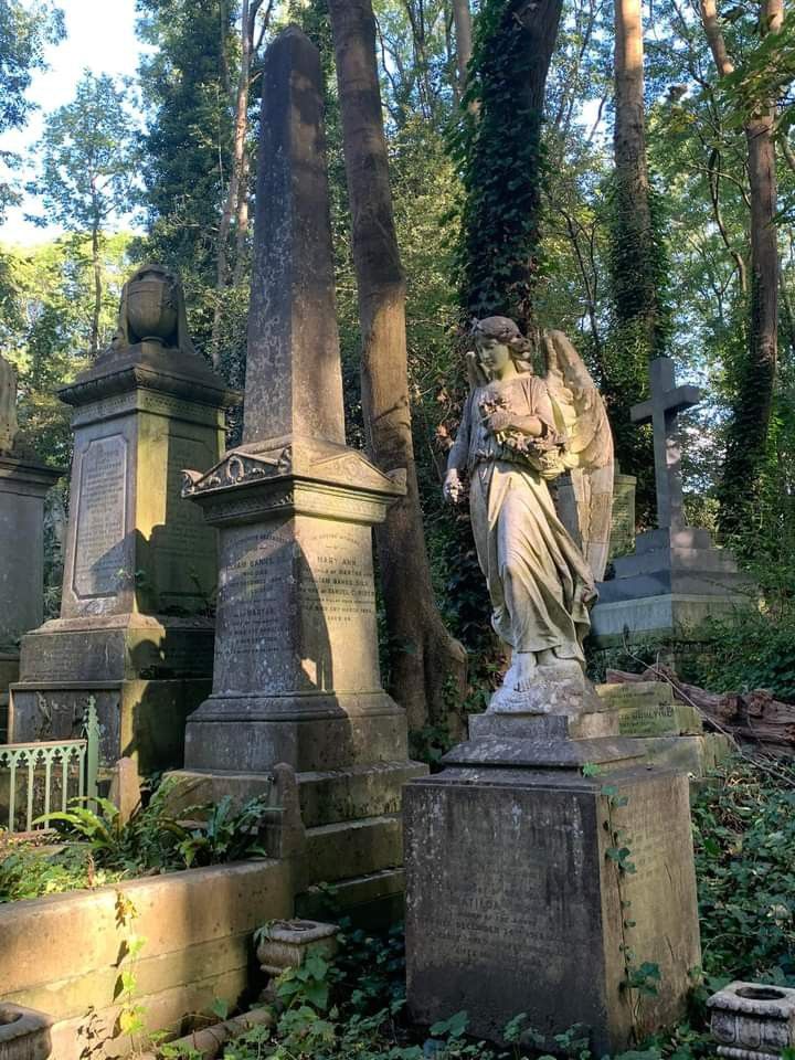 an old cemetery with statues and trees in the back ground, surrounded by greenery