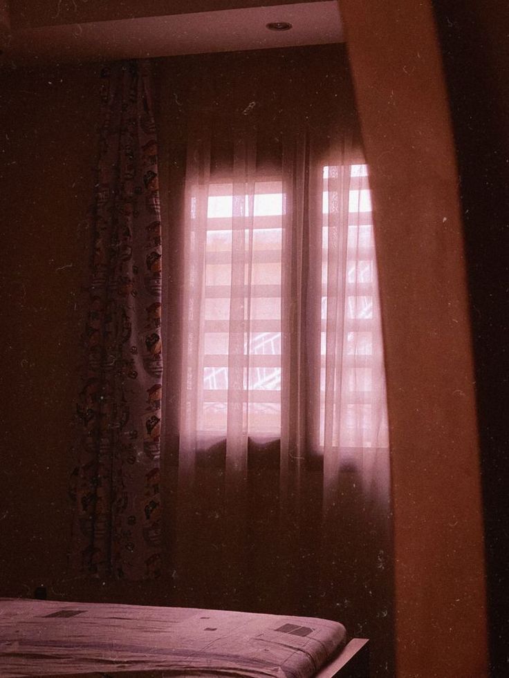 a bed sitting in front of a window with curtains on the side and a blanket on top of it