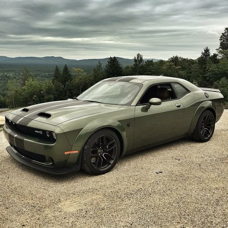 a green sports car parked on top of a gravel road next to trees and mountains