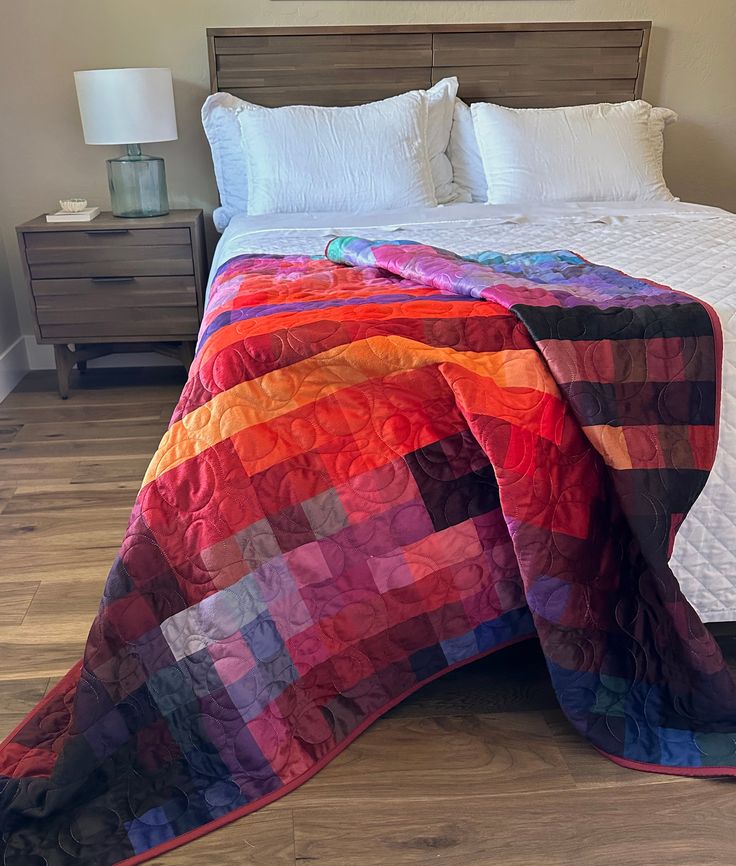 a bed with a colorful quilt on top of it next to a night stand and nightstand