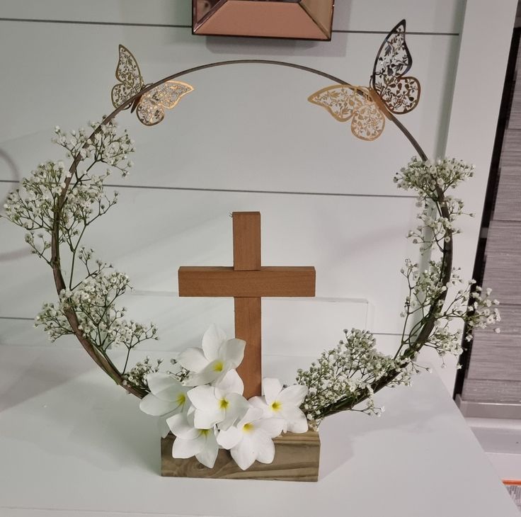 a cross with flowers and butterflies on it in front of a white wall behind the cross