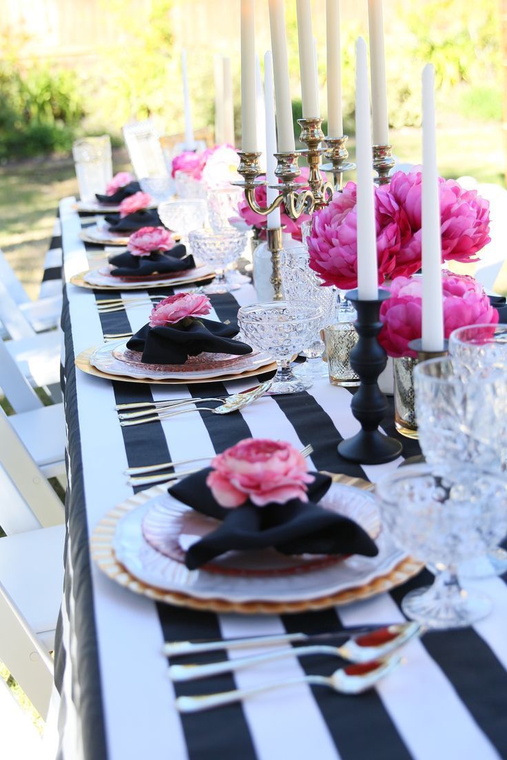 the table is set with black and white striped linens, candles, and pink flowers