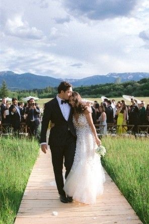 a bride and groom walking down a wooden walkway in front of an outdoor wedding ceremony