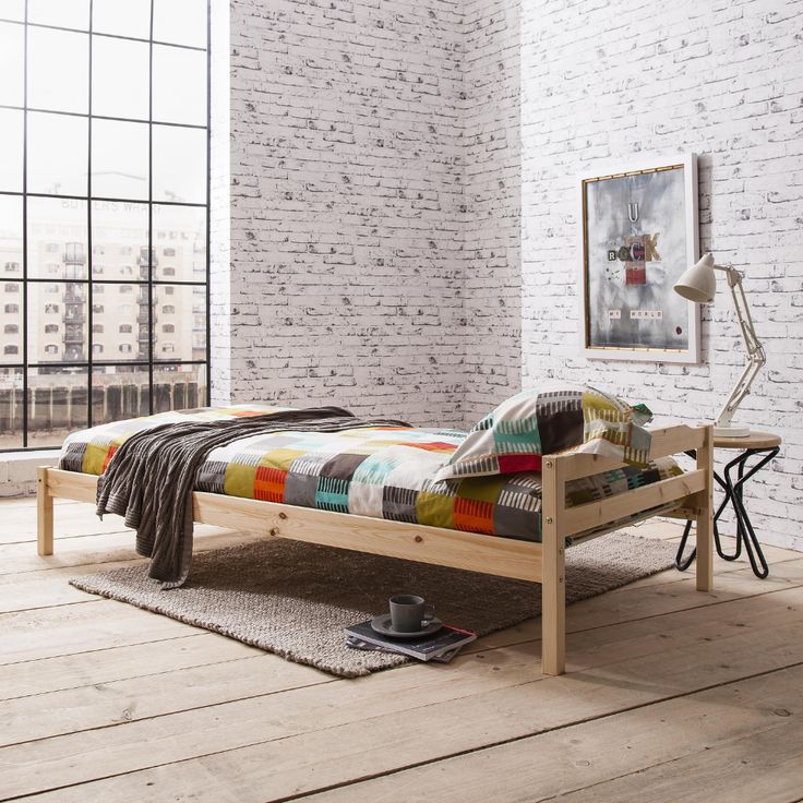 a bed sitting on top of a wooden floor next to a white brick wall in a bedroom