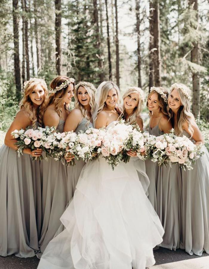 a group of women standing next to each other in front of trees and holding bouquets