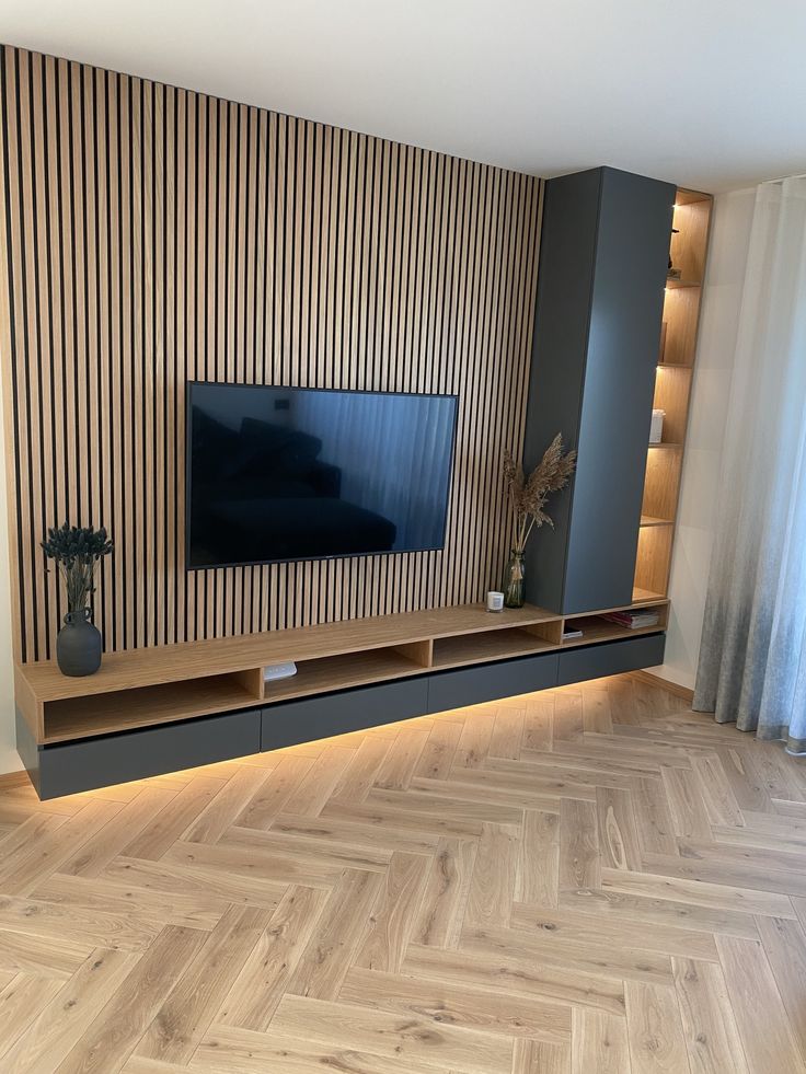 a living room with wood flooring and a large tv on the entertainment center wall