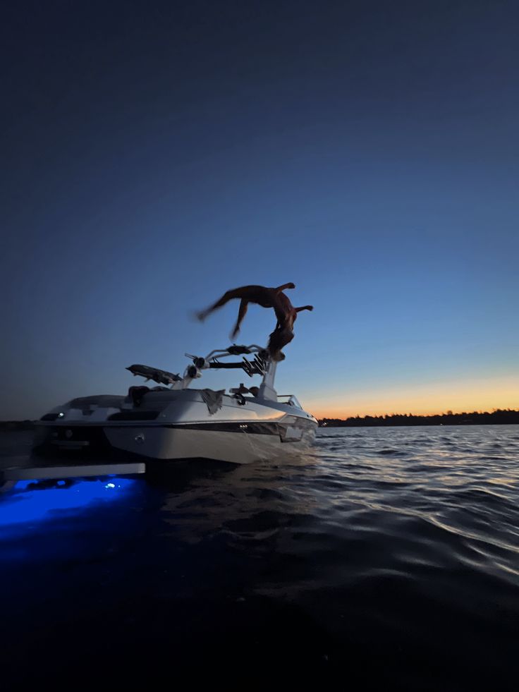 a man jumping off the back of a boat into the water at night with his feet in the air