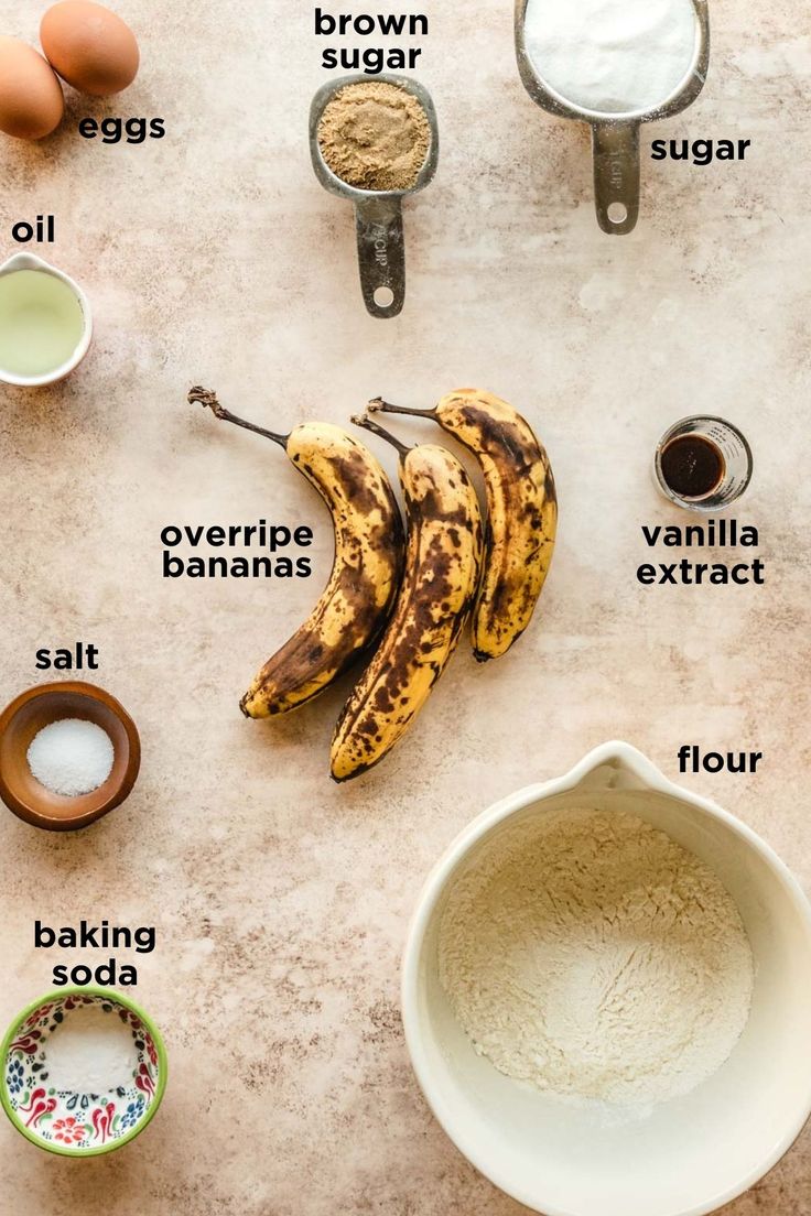 ingredients to make banana bread laid out on a table with bananas, eggs and flour