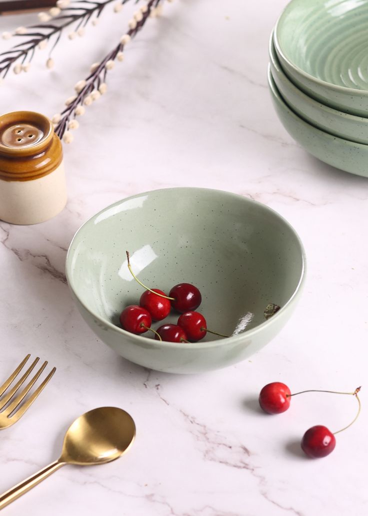 the bowl is filled with cherries on the table next to other plates and utensils