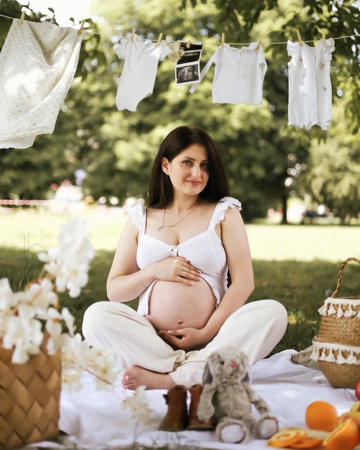 a pregnant woman sitting on the ground in front of some clothes hanging from a line