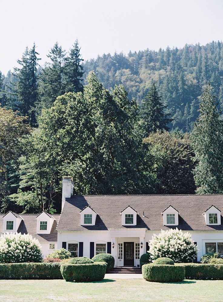 a large white house sitting in the middle of a lush green field next to trees