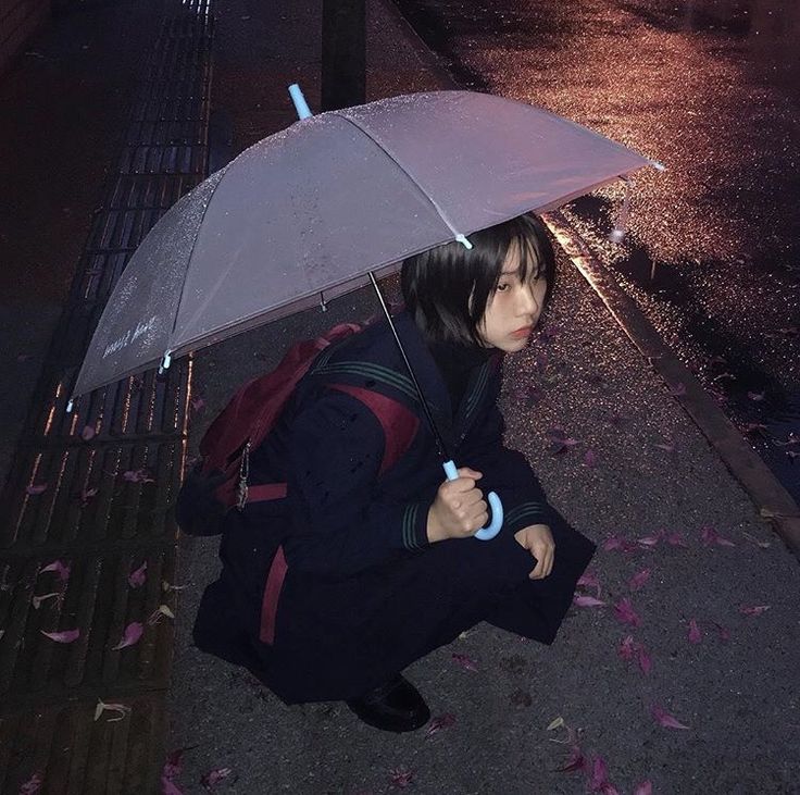 a woman sitting on the ground holding an umbrella over her head while it is raining