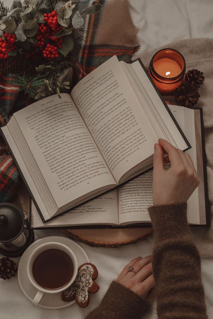 a person reading a book next to a cup of coffee and an open book on a bed