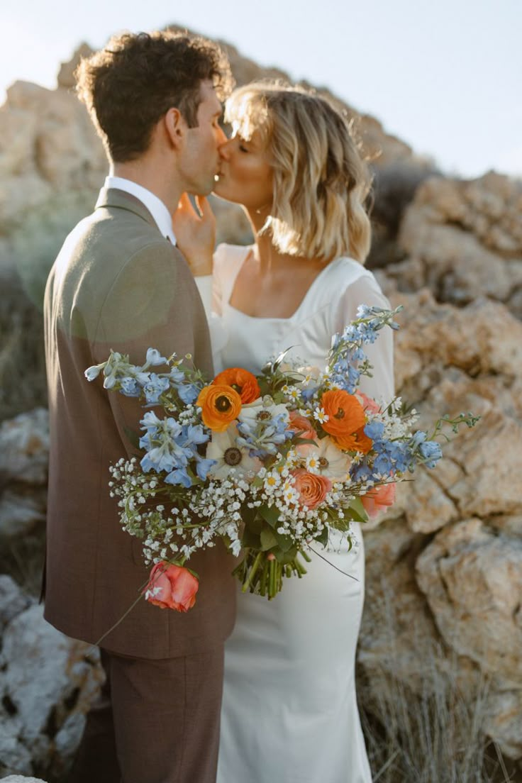 a bride and groom kissing in front of some rocks with flowers on their wedding day