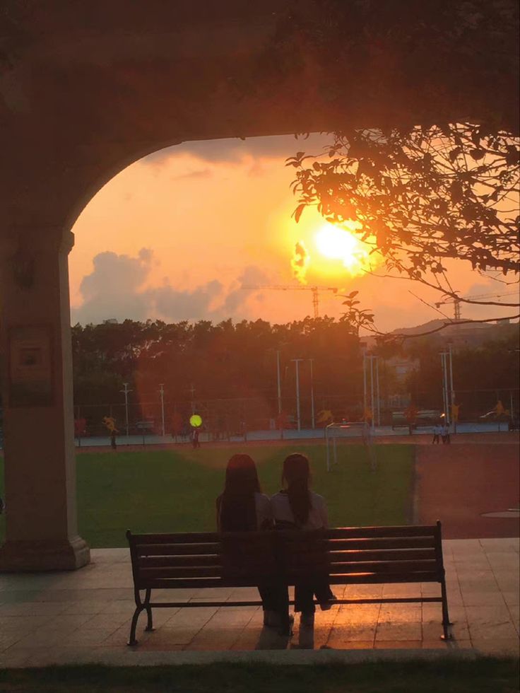 two people sitting on a bench watching the sun set