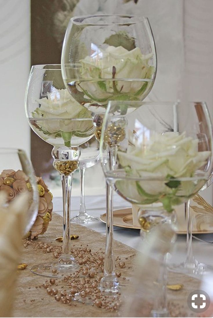 there are many wine glasses on the table with white flowers in them and one is empty