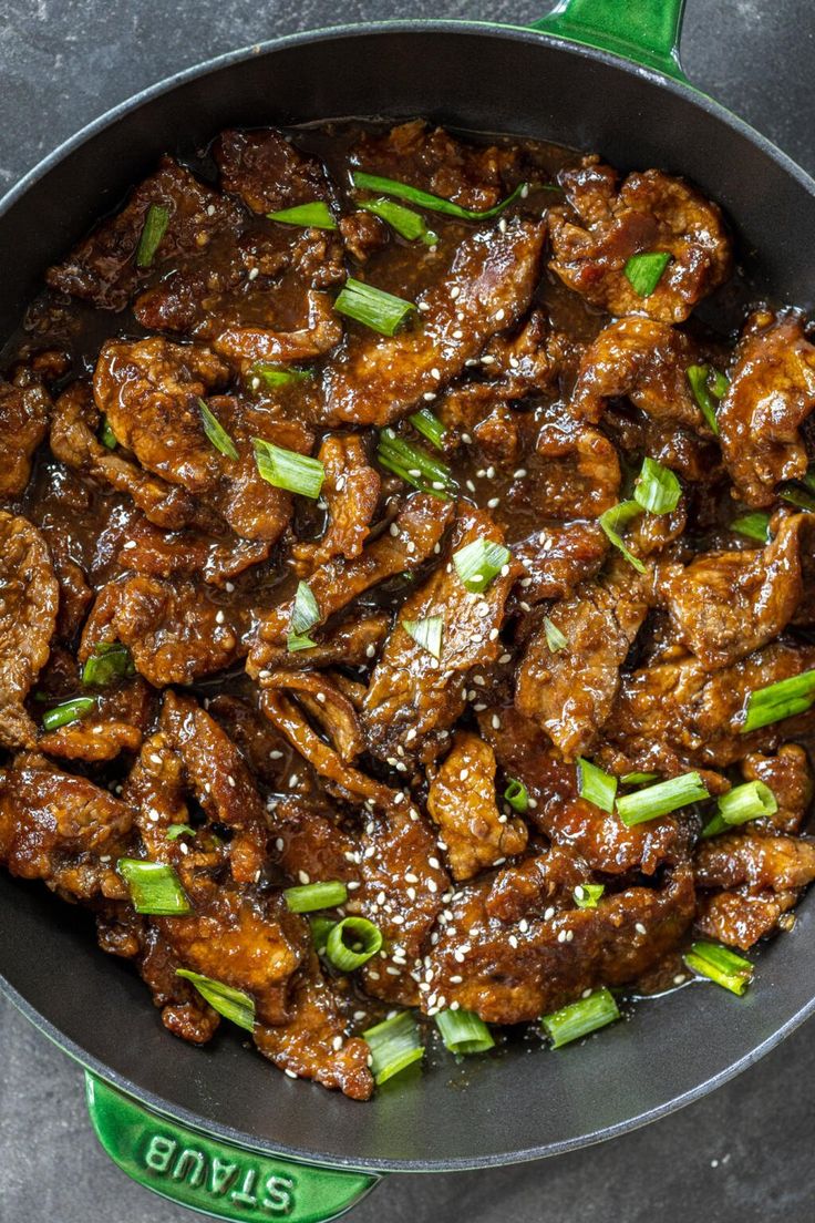 the meat is being cooked in a skillet with green onions and scallions