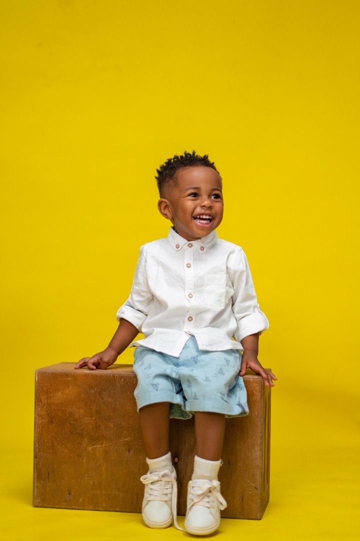 a little boy sitting on top of a wooden suitcase with his hands in his pockets