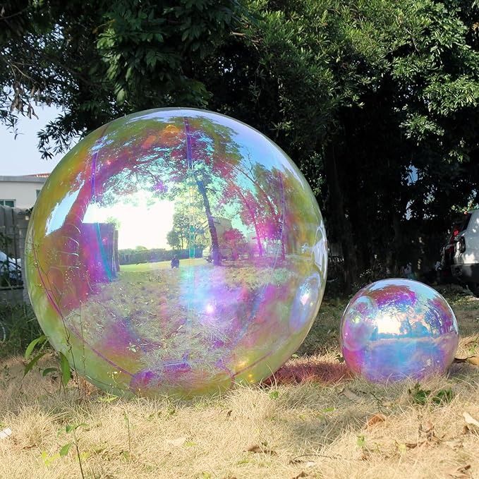 two large shiny balls sitting on the ground in front of some trees and grass,