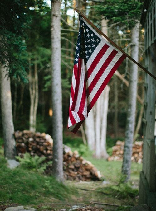 an american flag hanging from the side of a building in front of trees and rocks