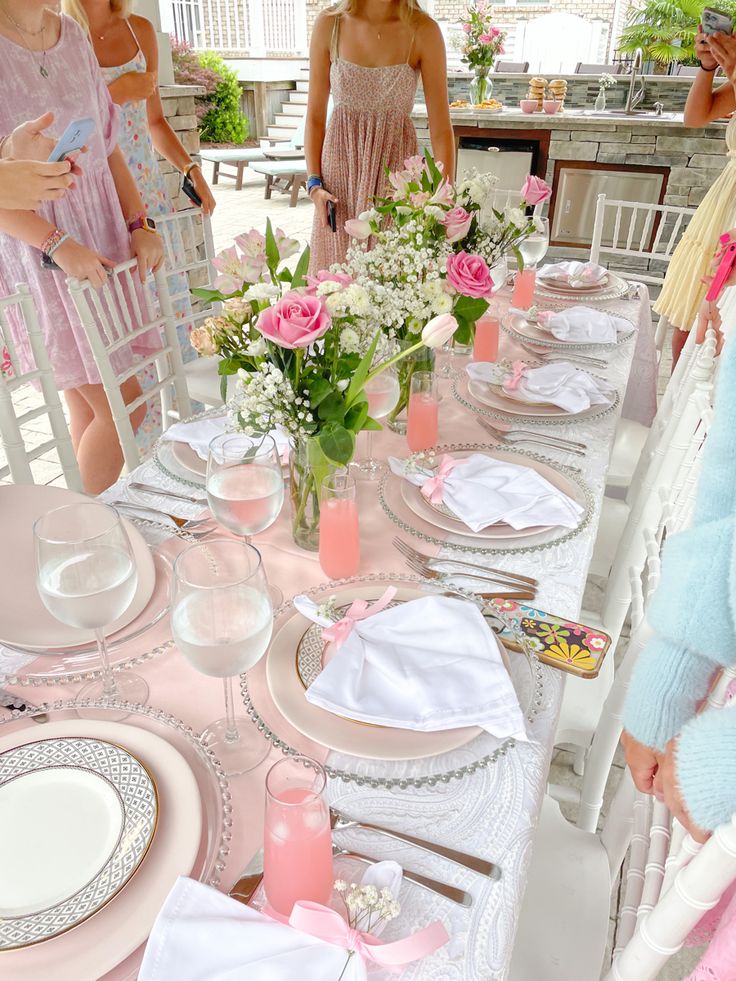 a group of girls standing around a table with pink and white flowers in vases