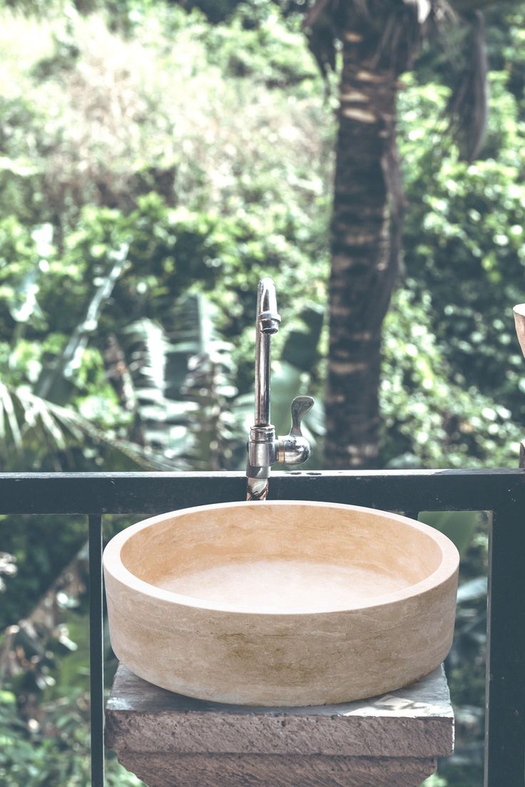 a bowl shaped sink sitting on top of a wooden table next to a forest filled with trees