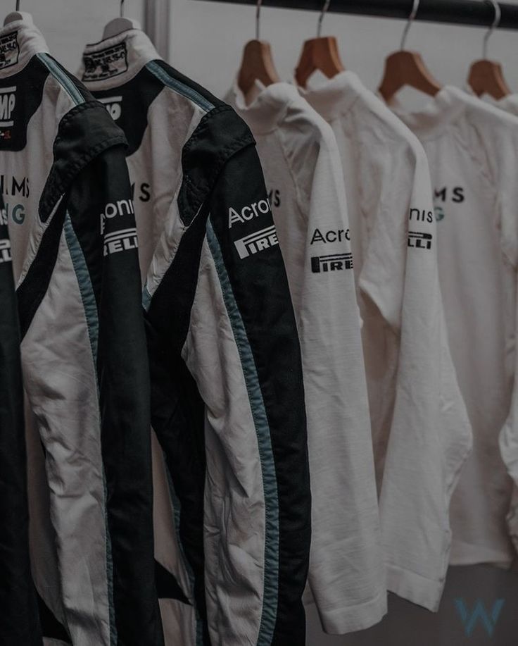 several racing jackets hanging on a rack in a shop or office area, with the words acro's printed on them