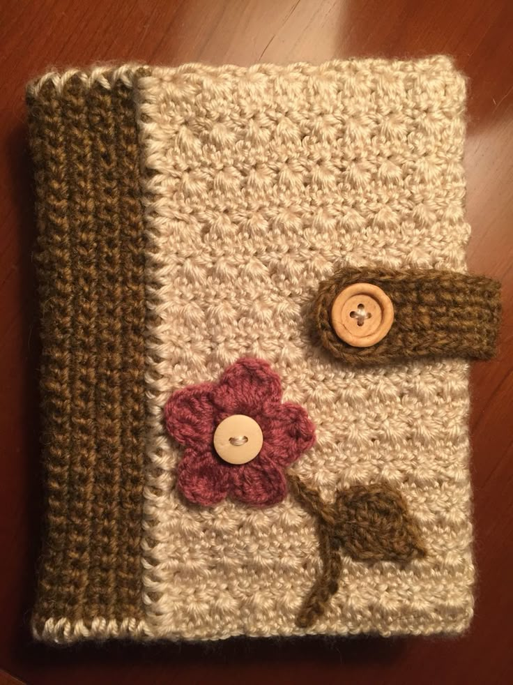 a crocheted book with buttons and a flower on the cover is sitting on a wooden table