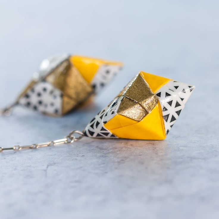 two yellow and white origami earrings hanging from a chain on a gray surface