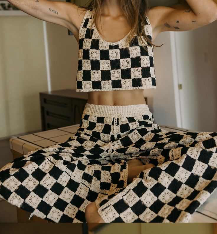 a woman sitting on top of a bed wearing black and white checkered pants with her hands behind her head