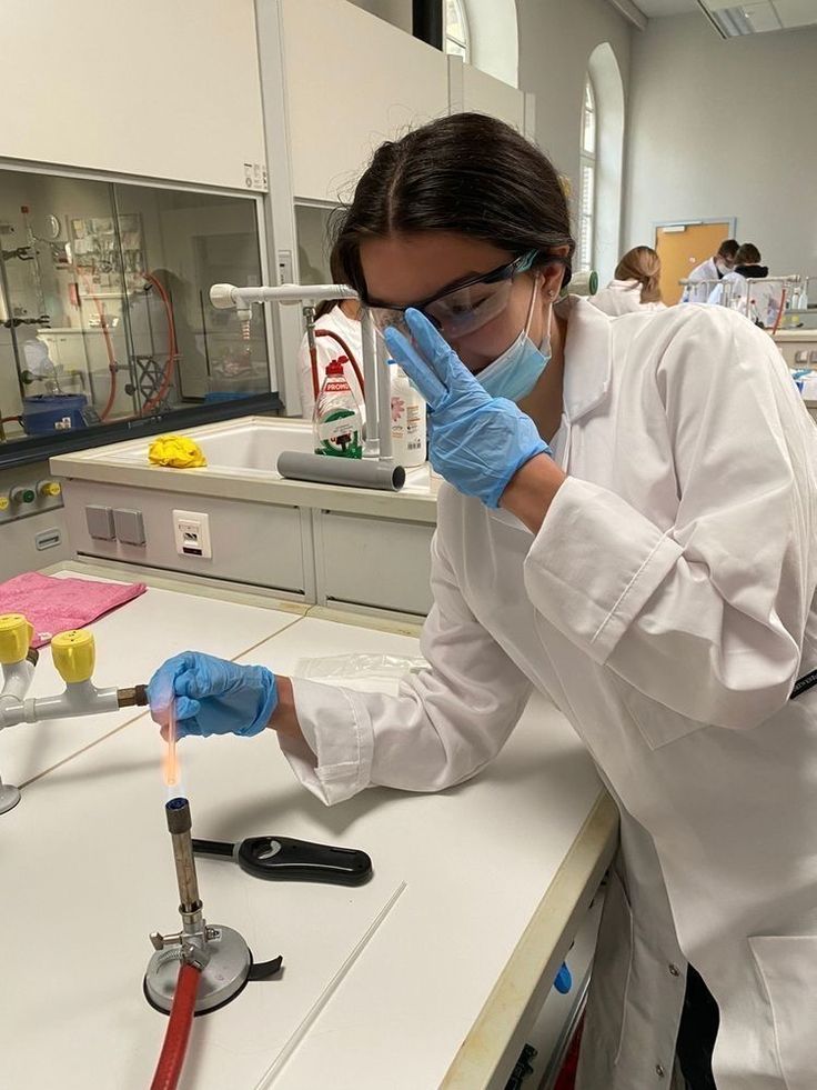 a woman in white lab coat and blue gloves holding a pipe with liquid on it