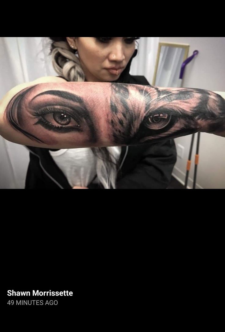 a woman with her arm covered in black and grey ink, has an eye tattoo on it