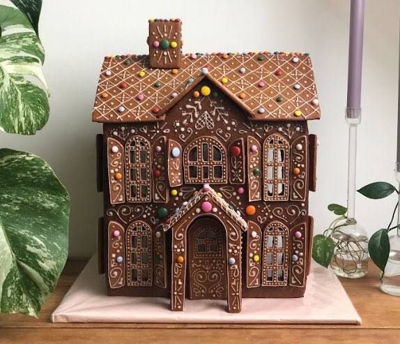 a gingerbread house is on a table next to a potted plant and candle