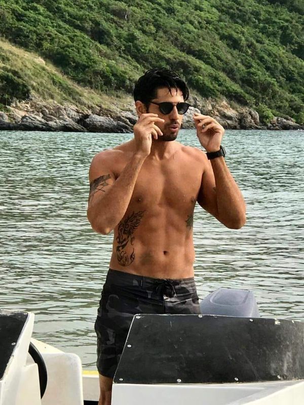 a shirtless man on a boat talking on his cell phone while standing in the water