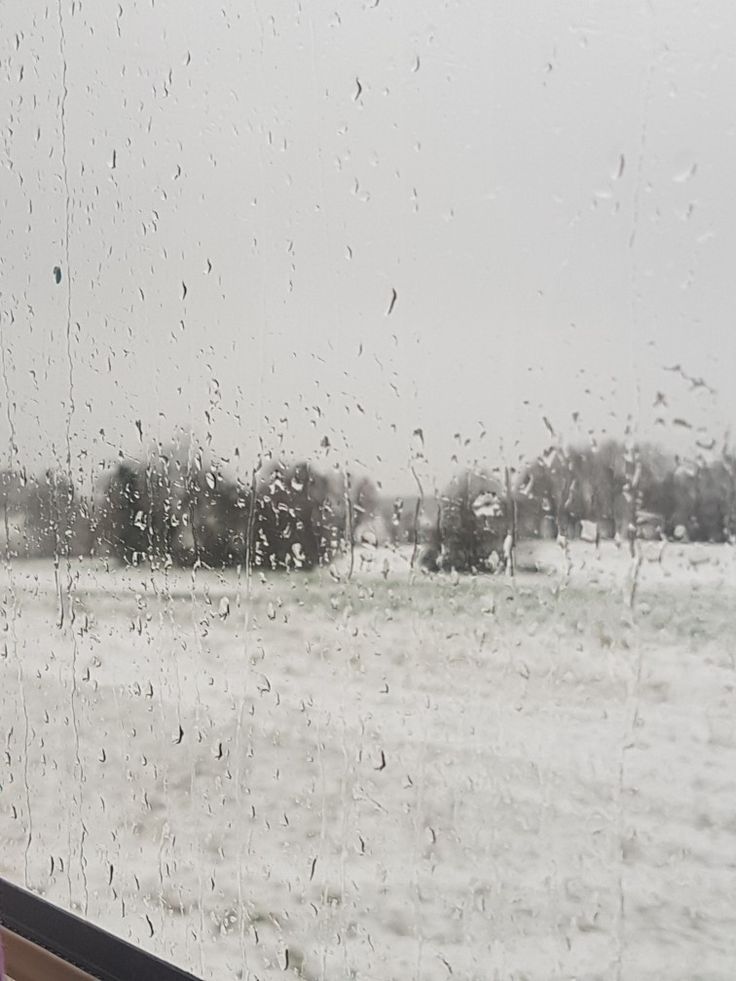 a window with rain drops on it looking out at a field in the distance and trees