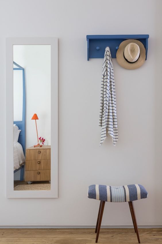 a blue and white bench sitting in front of a mirror next to a hat rack