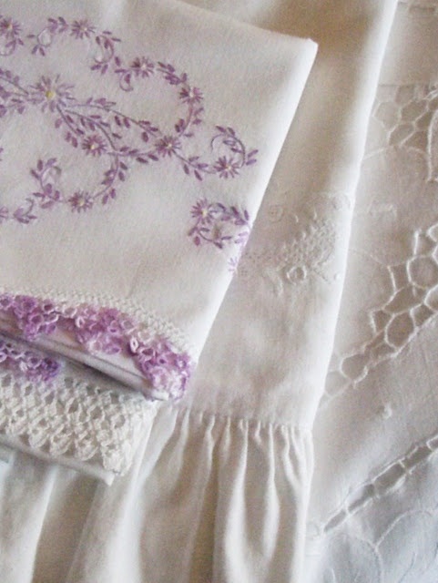 two pieces of white linen with purple flowers and lace on them are laying next to each other