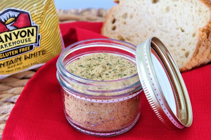 an open jar of peanut butter next to a loaf of bread on a red cloth