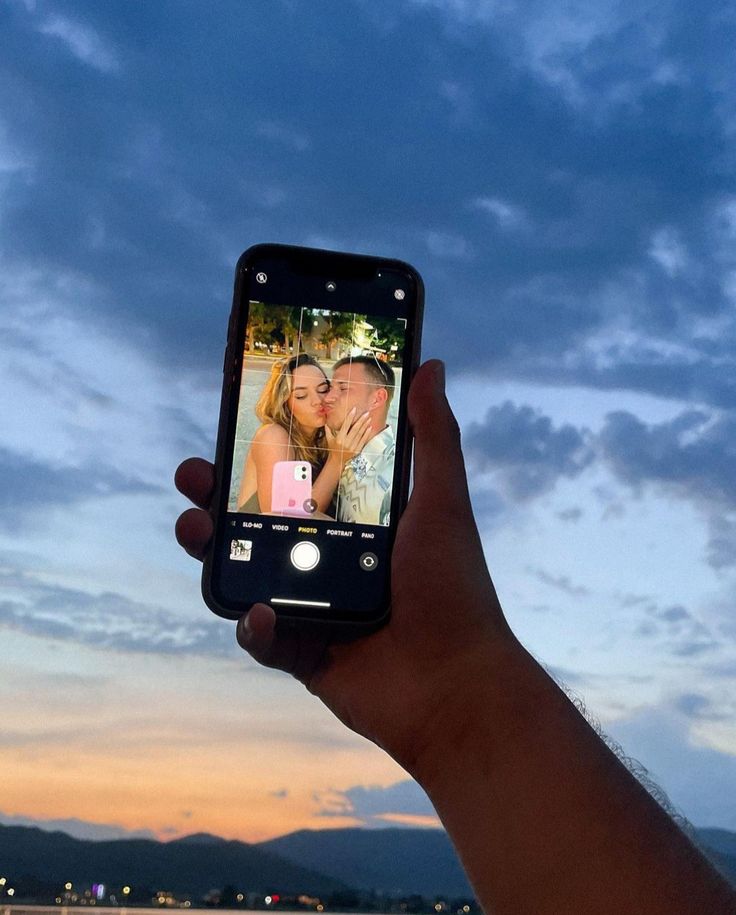 a person holding up a cell phone to take a photo with the sky in the background