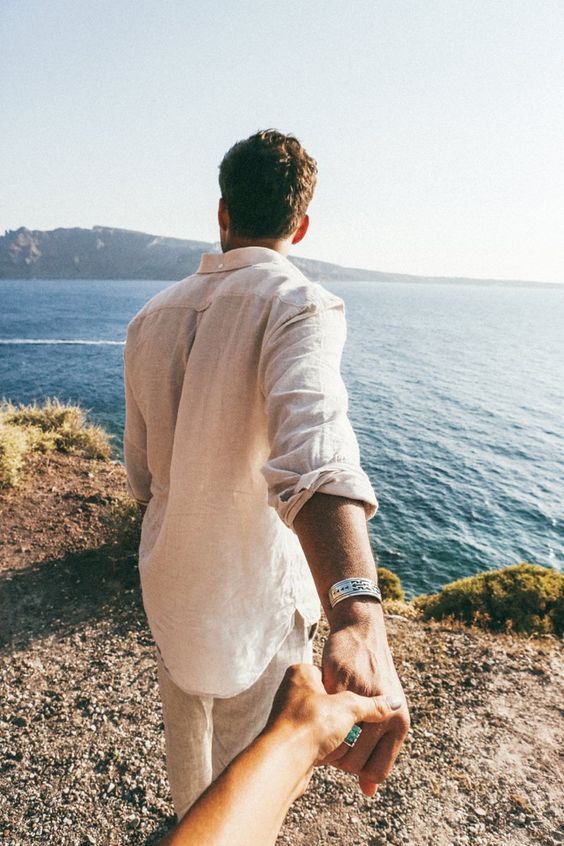 a man holding the hand of another person on top of a hill by the ocean