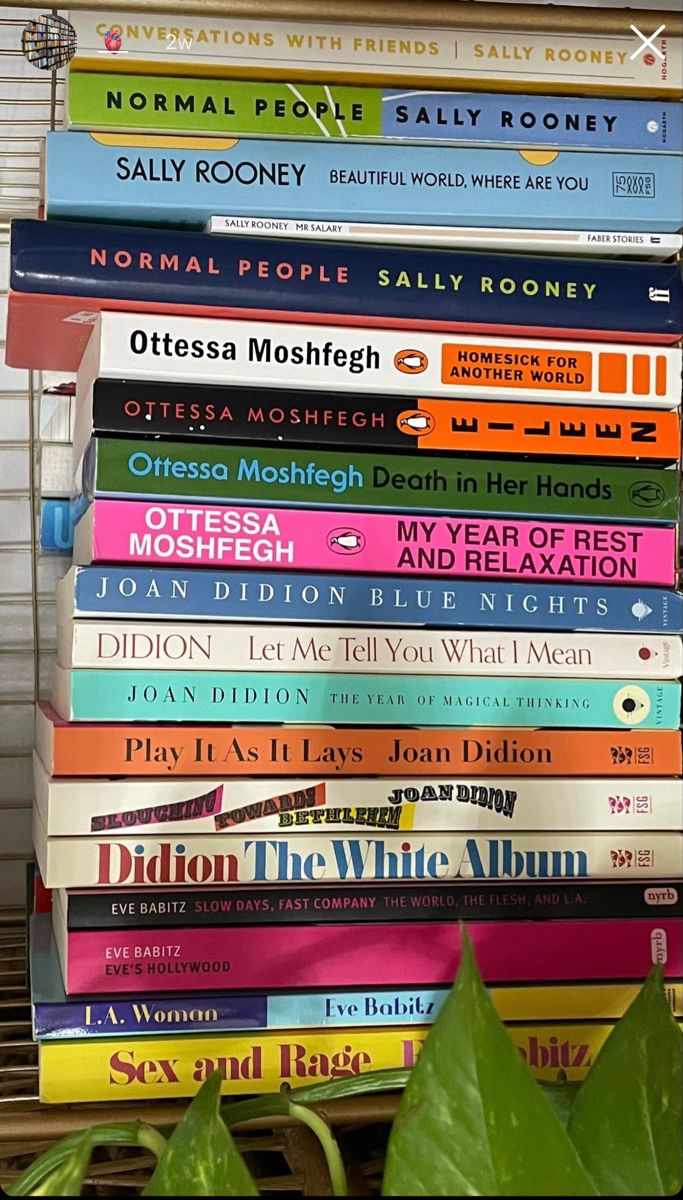 a stack of books sitting on top of a wooden table next to a green plant