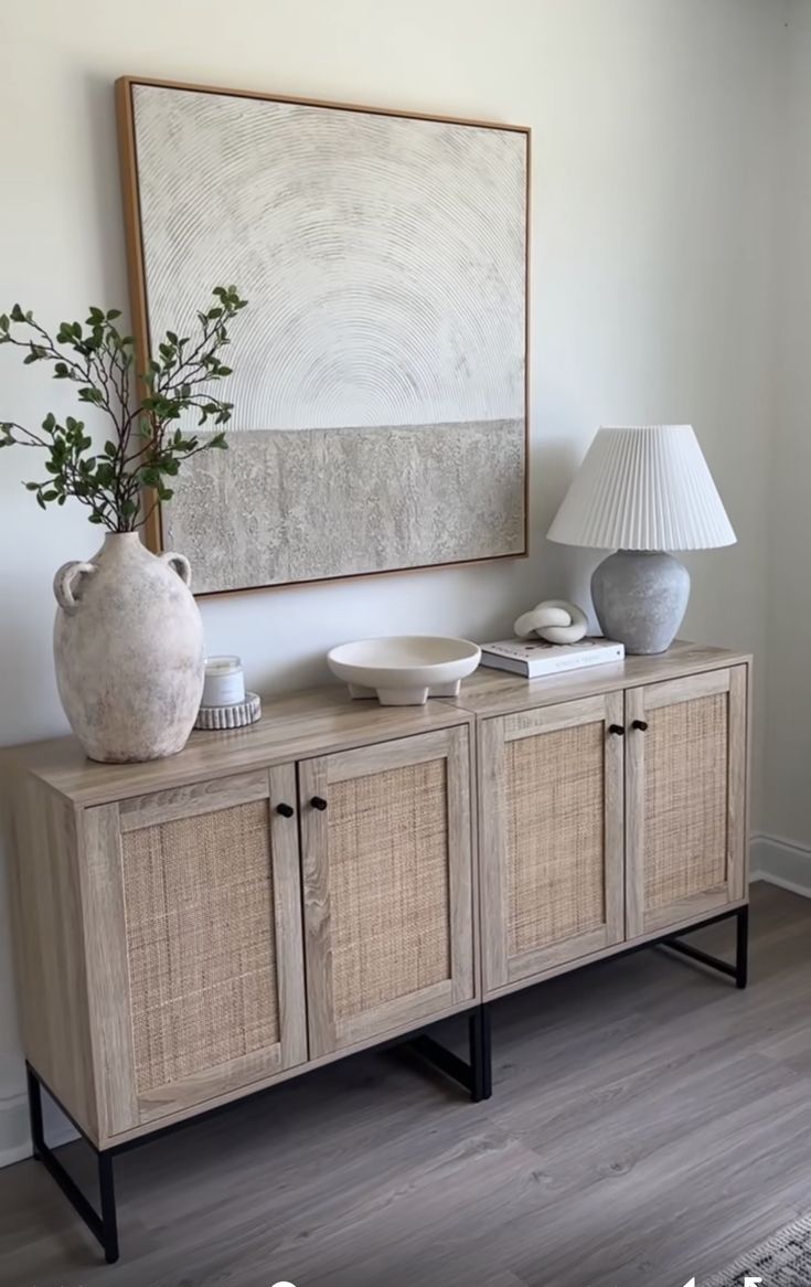 a white vase sitting on top of a wooden cabinet next to a lamp and painting