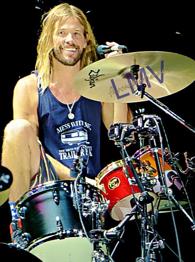 a man with long hair sitting on the drums in front of a drum set and microphone