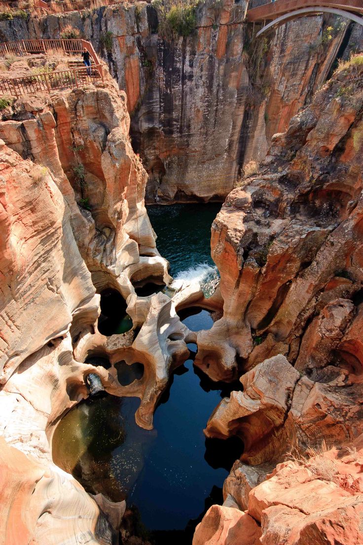 a bridge over a river surrounded by large rocks and water in the middle of a canyon